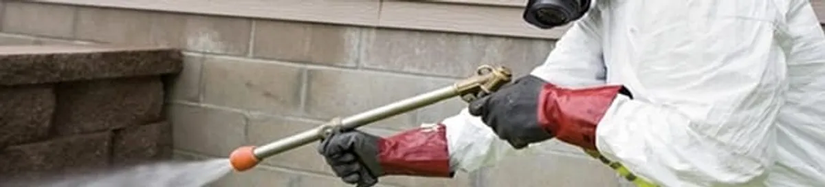 Pest control technician applying exterior insect treatment along a home foundation in San Antonio, TX