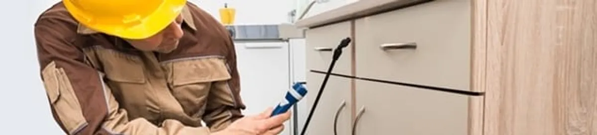 Roach exterminator applying treatment under kitchen cabinets in San Antonio, TX