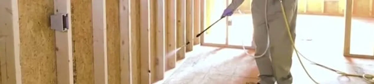 Termite treatment technician applying spray along framing and unfinished walls in San Antonio, TX